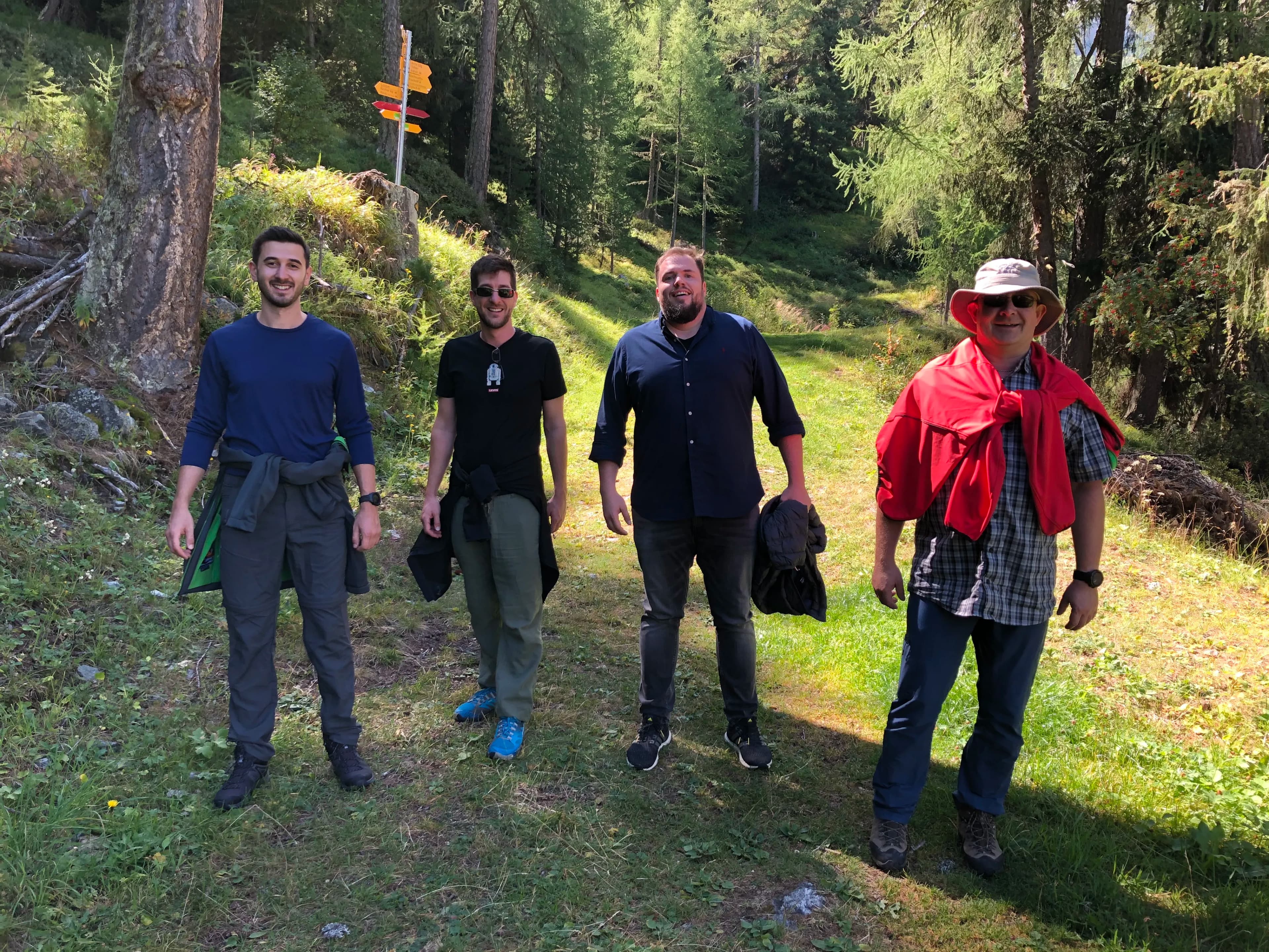 Previse guys smiling on a sunny forest trail, with trees in the background.