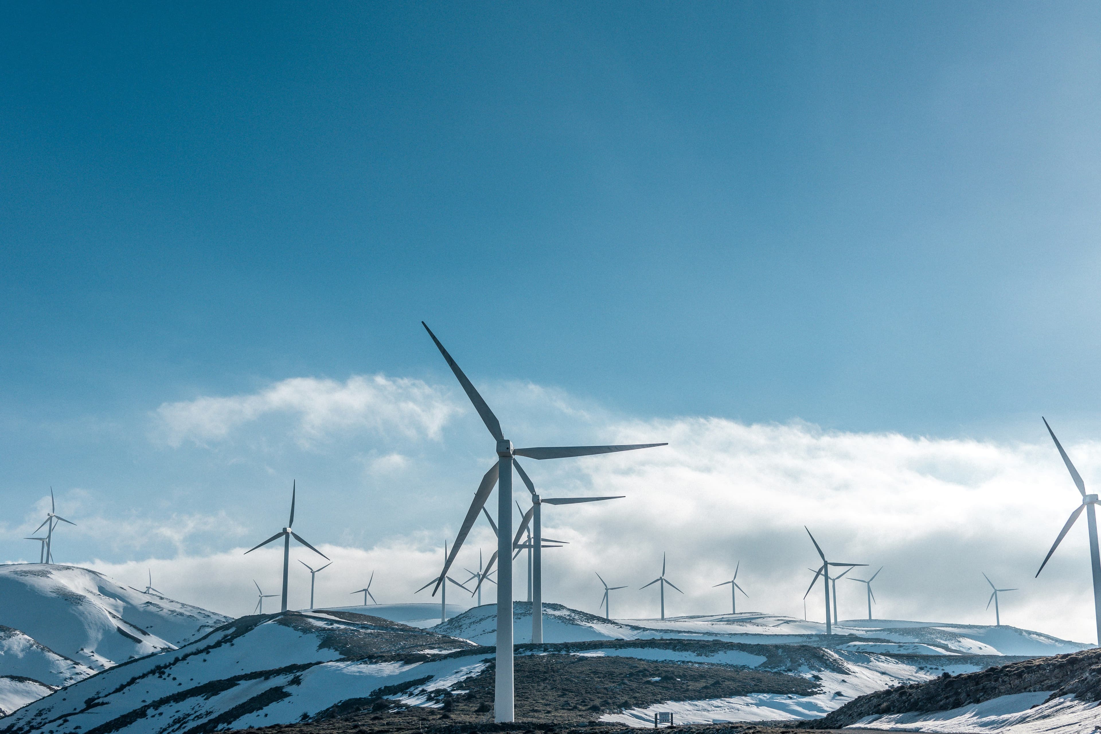 Wind turbines on snowy hills under a clear blue sky, generating renewable energy.